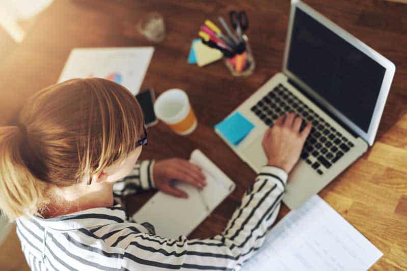 Woman with glasses taking notes and working on a laptop
