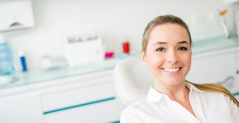 A smiling blonde woman sits in a dental chair