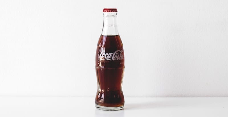 Glass bottle of Coca-Cola soda with a red lid against a white background