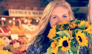 Blonde woman covers her mouth with a bouquet of sunflowers at a Farmers Market