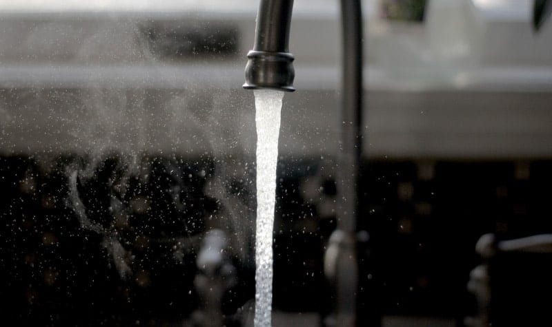 Closeup of a stream of fluoridated tap water coming from a kitchen faucet