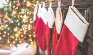 Closeup of a line of red and white stockings hanging from the fireplace mantle in front of a Christmas tree